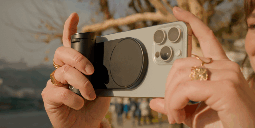 Main tenant un smartphone avec objectif attaché.