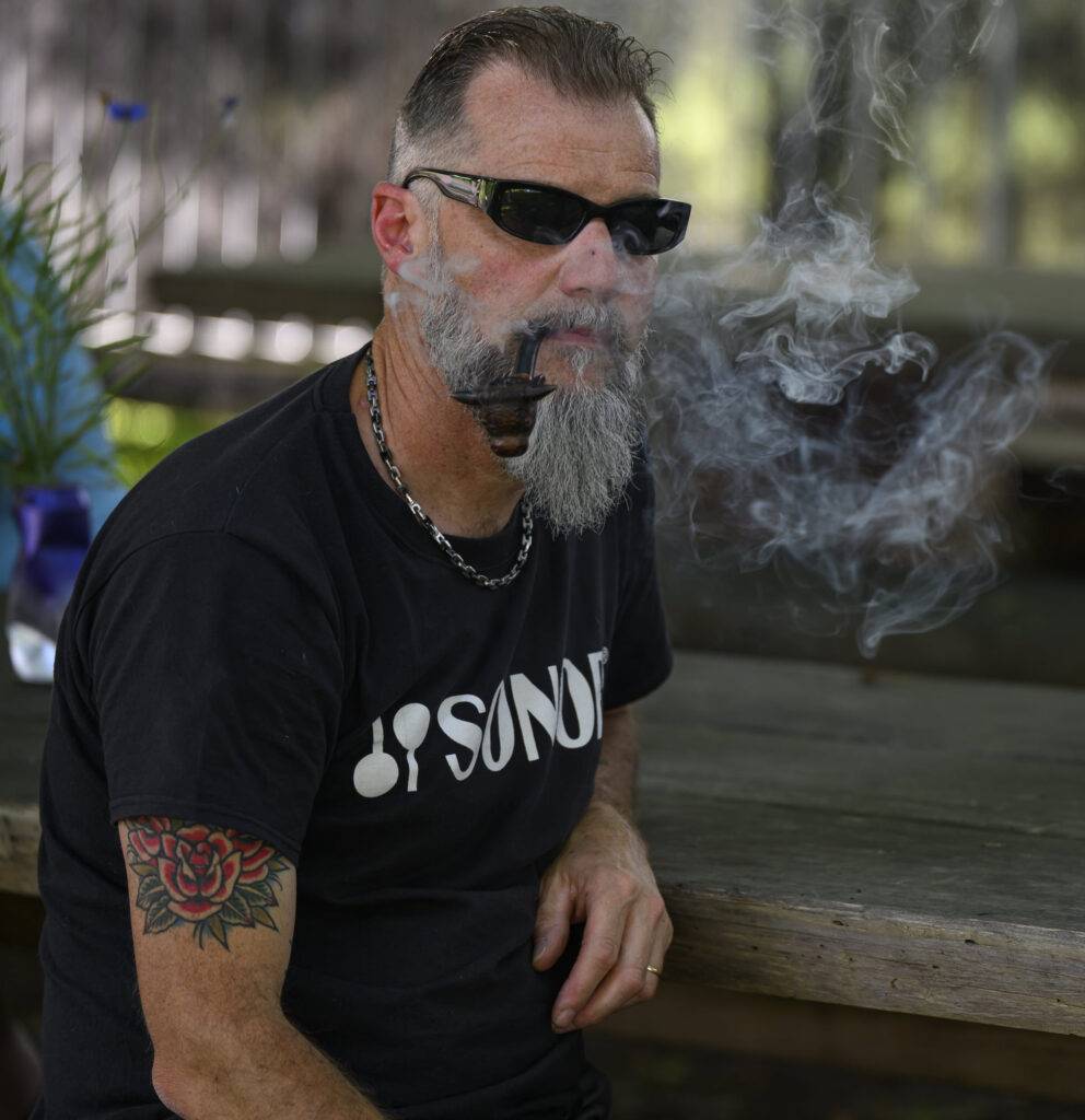 Homme barbu fumant une pipe en plein air.