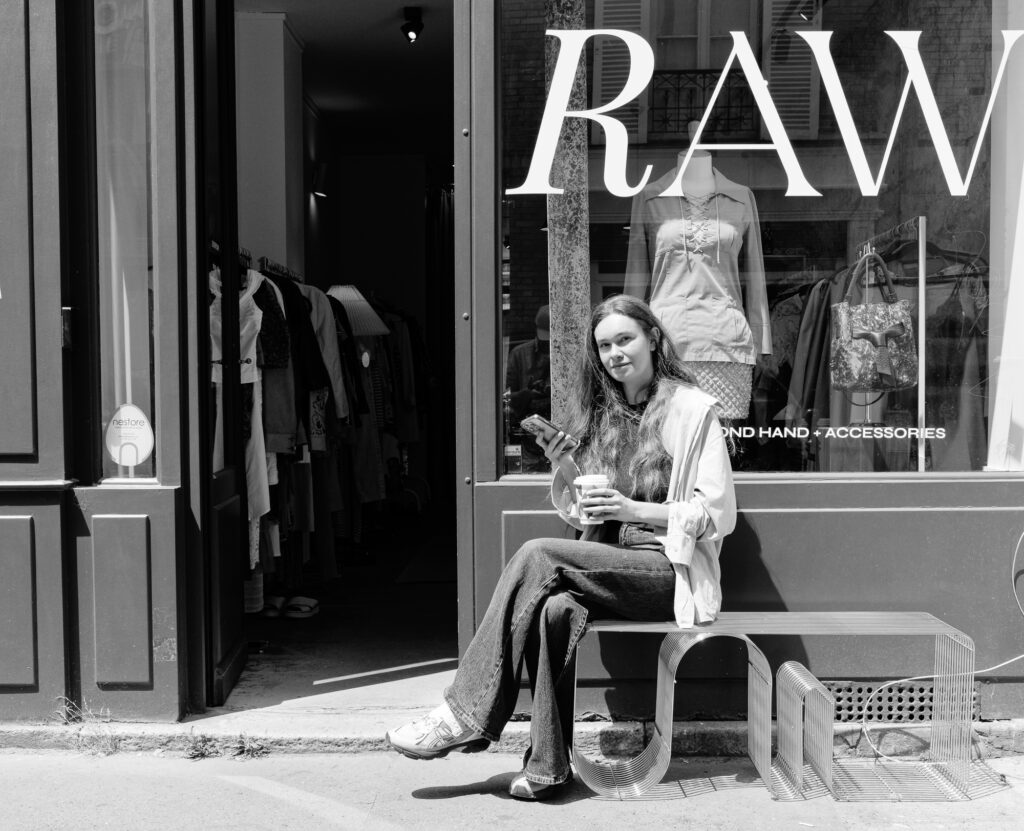 Femme assise devant une boutique avec un café.