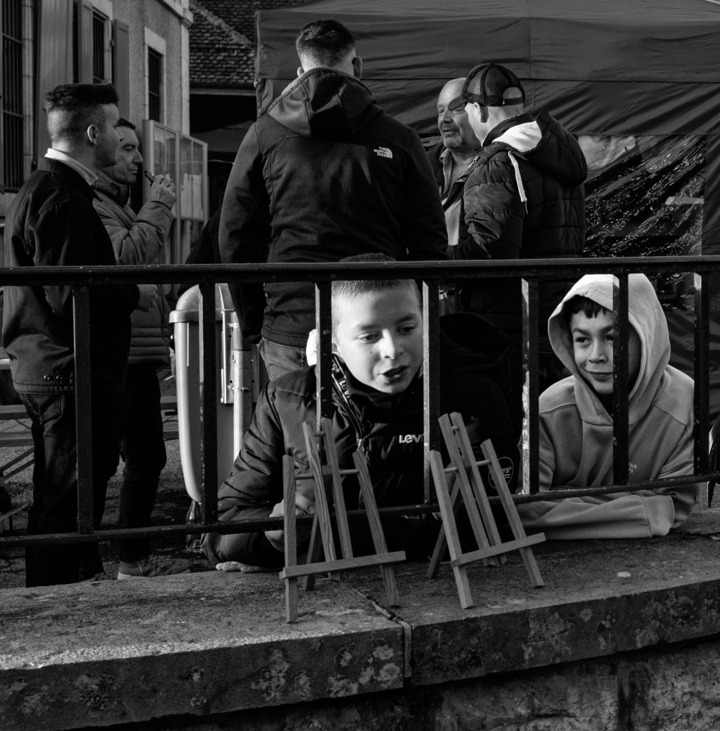 Enfants observant des chevalets devant marché extérieur, noir et blanc.