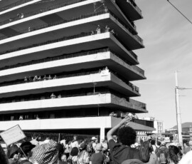 Manifestation devant immeuble moderne, spectateurs aux balcons
